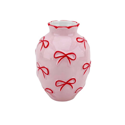 Vaso rosa alto com laços vermelhos decorativos.