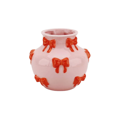 Vaso rosa arredondado com laços vermelhos decorativos.